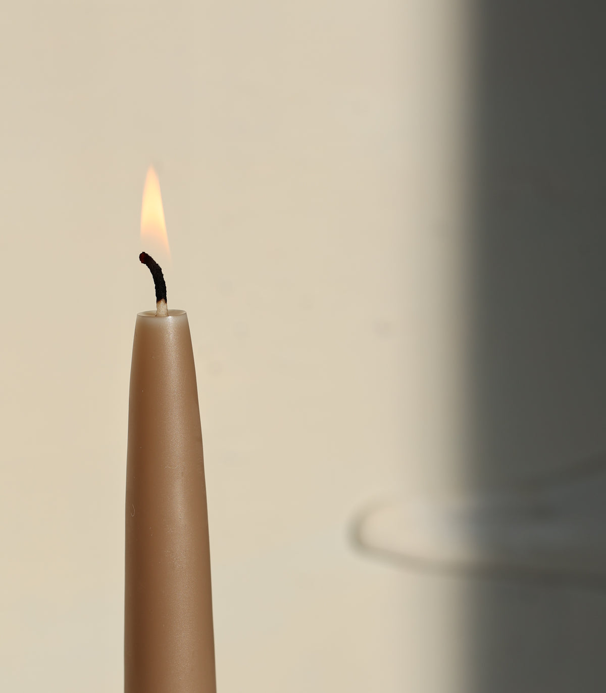 A single taupe GLŌAM Classic Beeswax Taper burning against a soft neutral background.