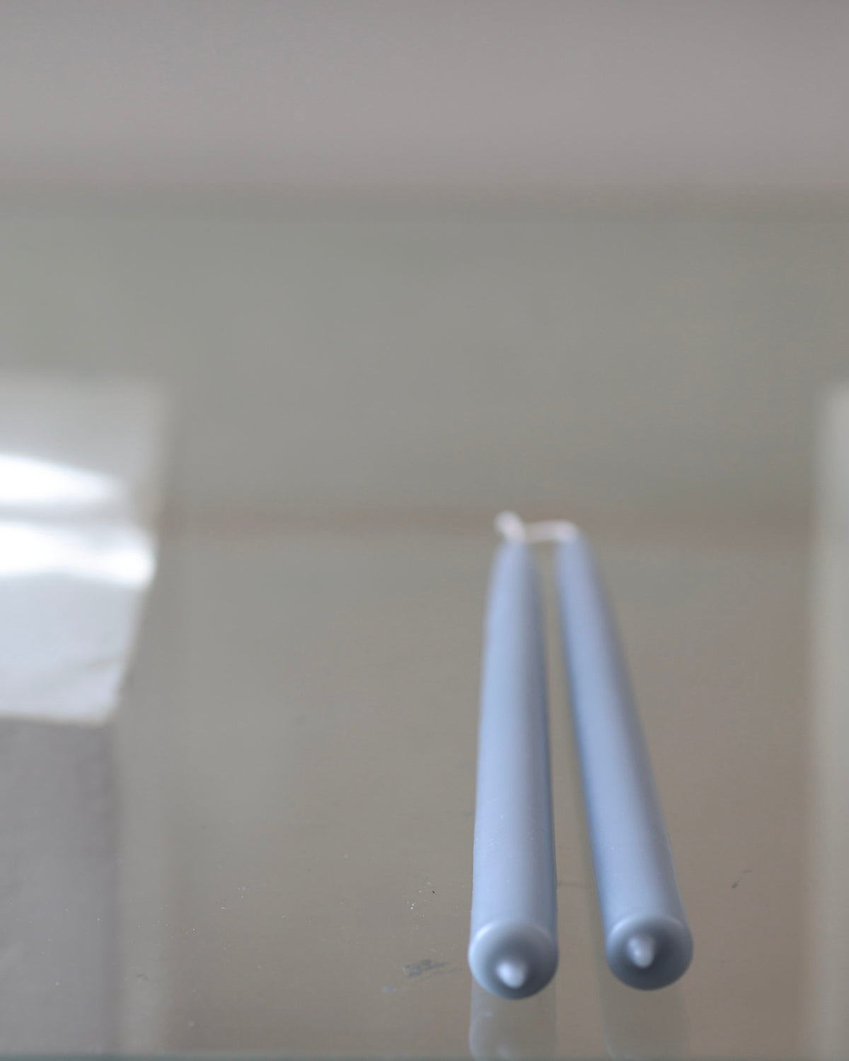 Close-up of two pale blue GLŌAM Classic Beeswax Tapers, showing their rounded ends against a softly blurred background.