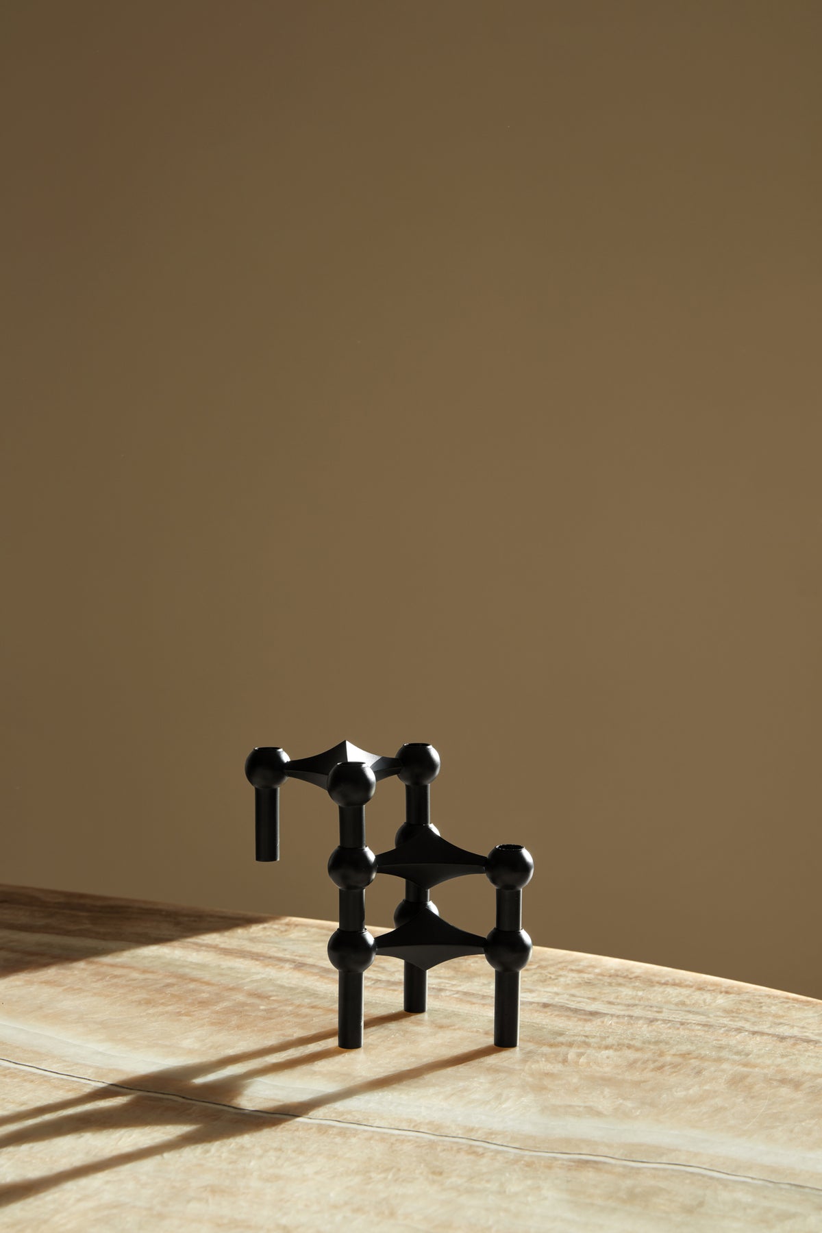 STOFF Nagel black candle holders stacked into a sculptural composition on a travertine surface in warm light