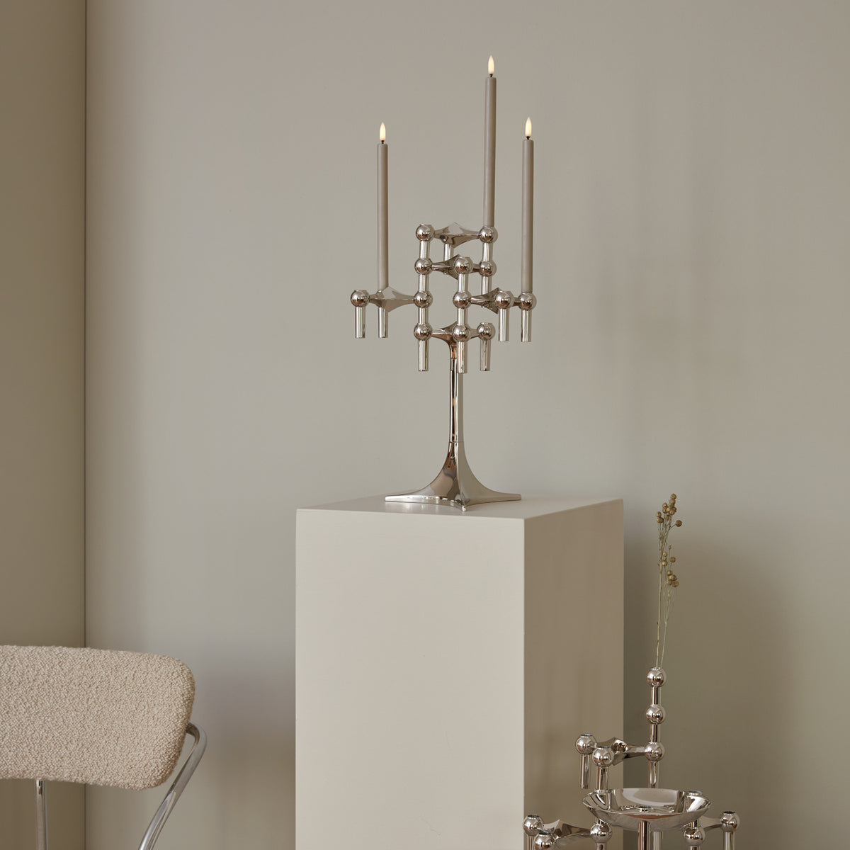 STOFF Nagel chrome stand holding lit taper candles on a plinth in a modern interior