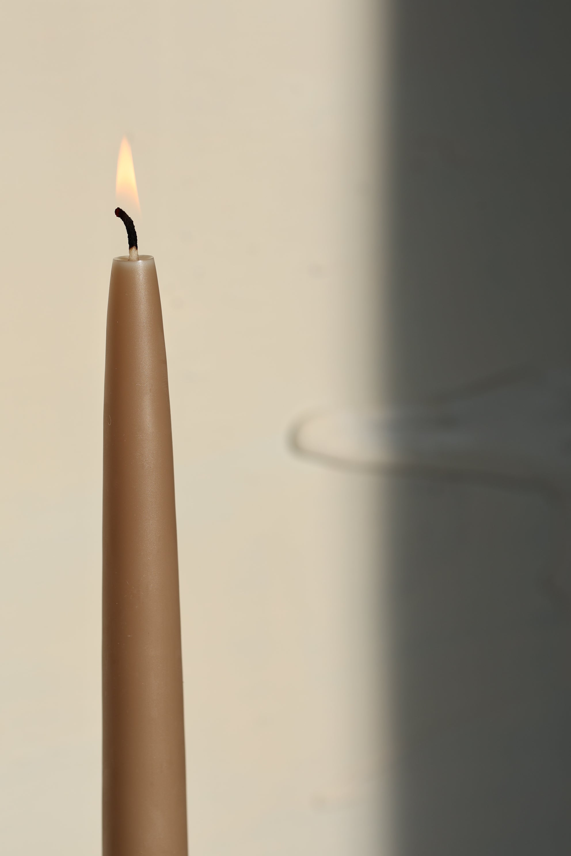 A single taupe GLŌAM Classic Beeswax Taper burning against a soft neutral background.