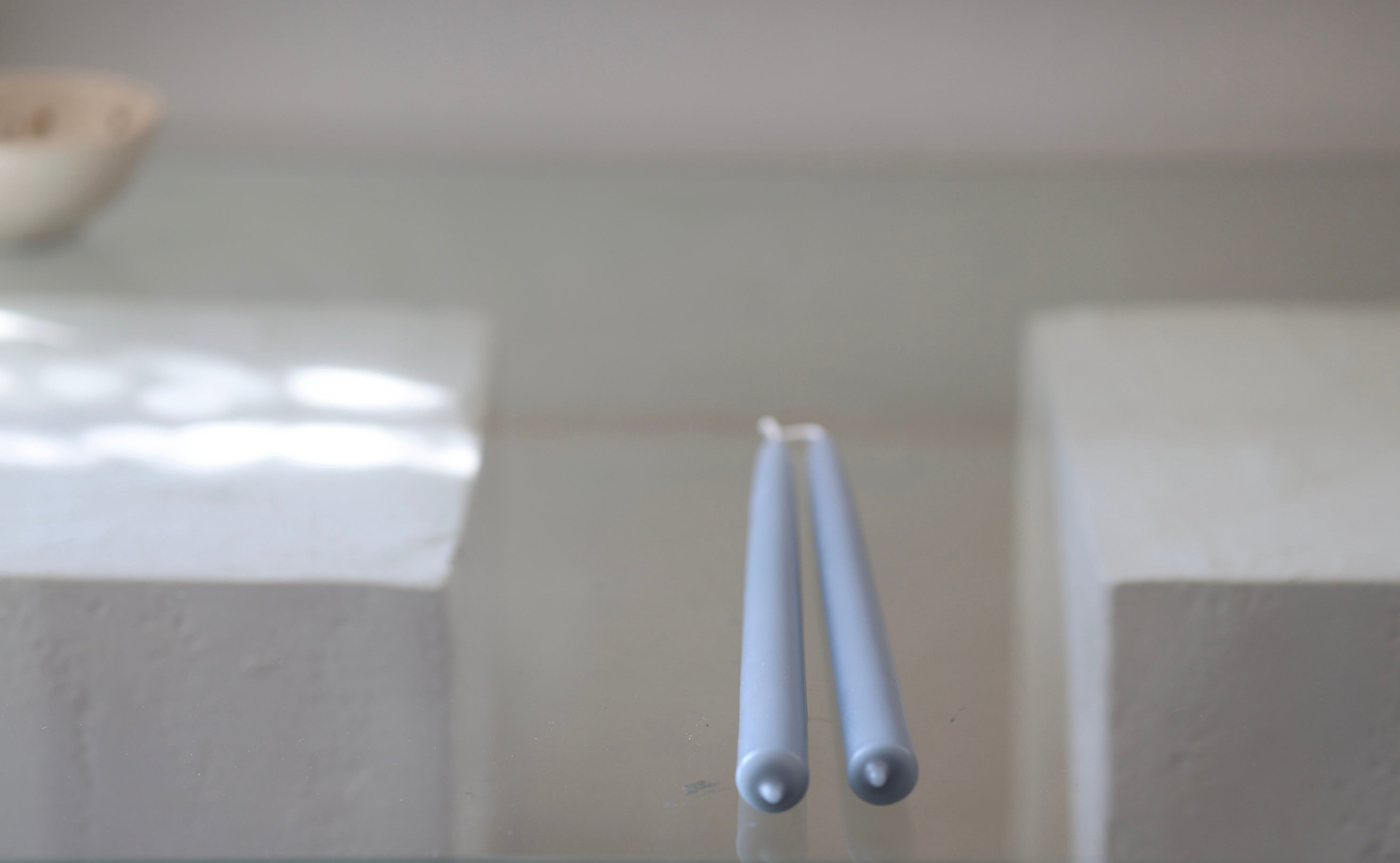 Close-up of two pale blue GLŌAM Classic Beeswax Tapers, showing their rounded ends against a softly blurred background.