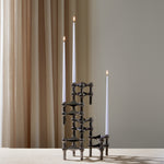 STOFF Nagel black candle holders holding three lit taper candles on a travertine surface against a soft curtain