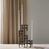 STOFF Nagel black candle holders holding three lit taper candles on a travertine surface against a soft curtain