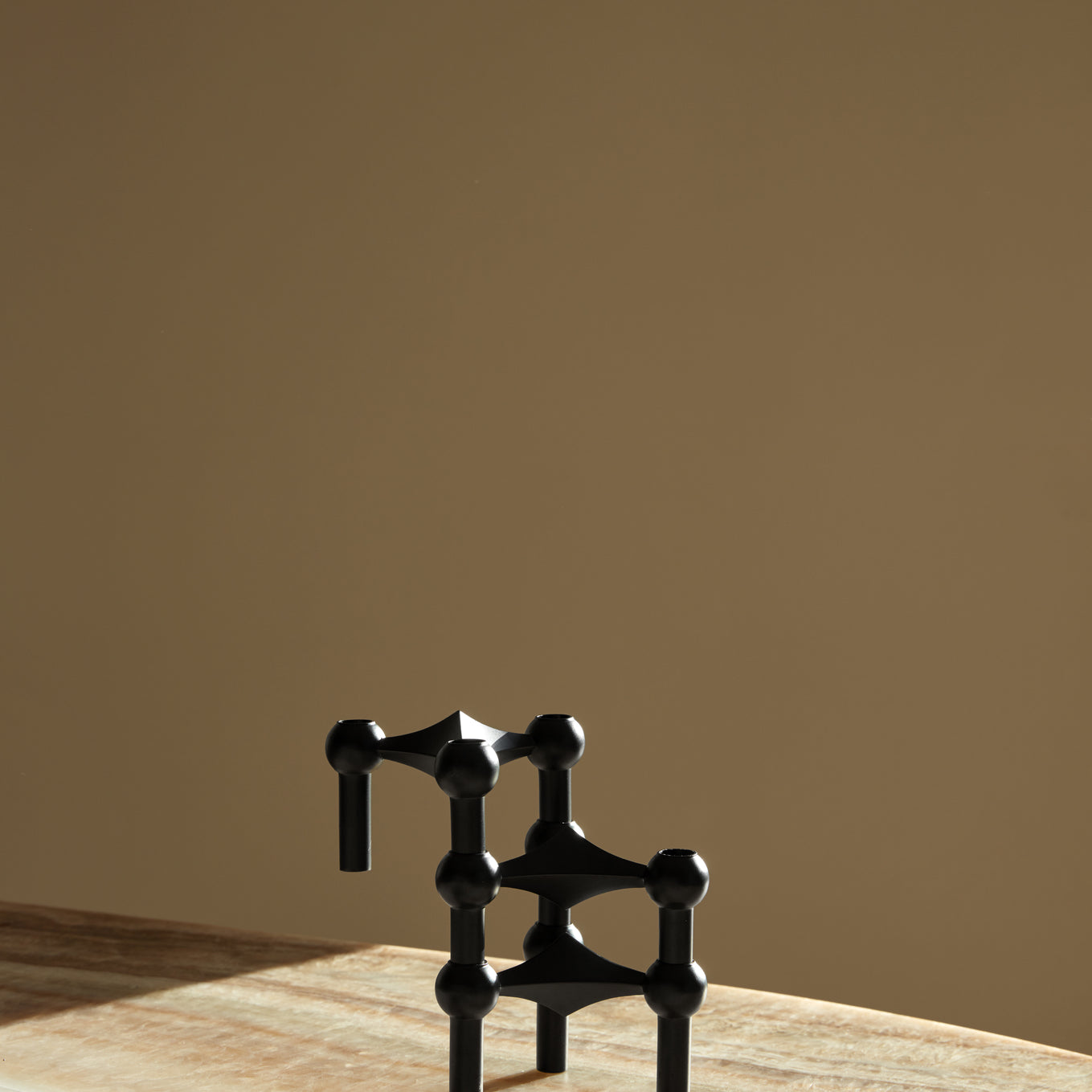 STOFF Nagel black candle holders stacked into a sculptural composition on a travertine surface in warm light