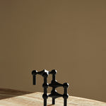 STOFF Nagel black candle holders stacked into a sculptural composition on a travertine surface in warm light