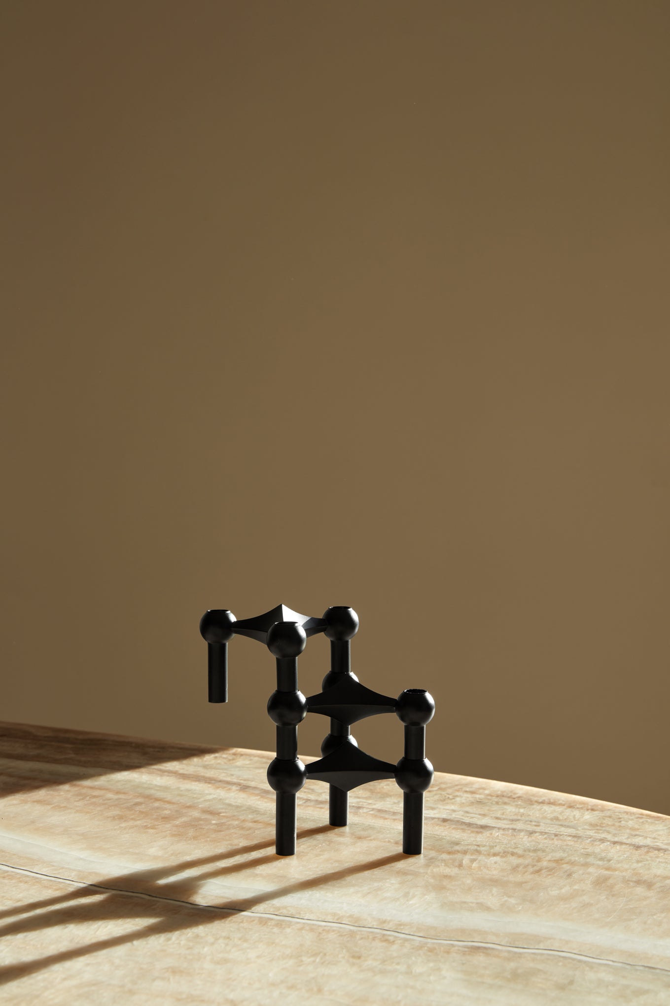STOFF Nagel black candle holders stacked into a sculptural composition on a travertine surface in warm light