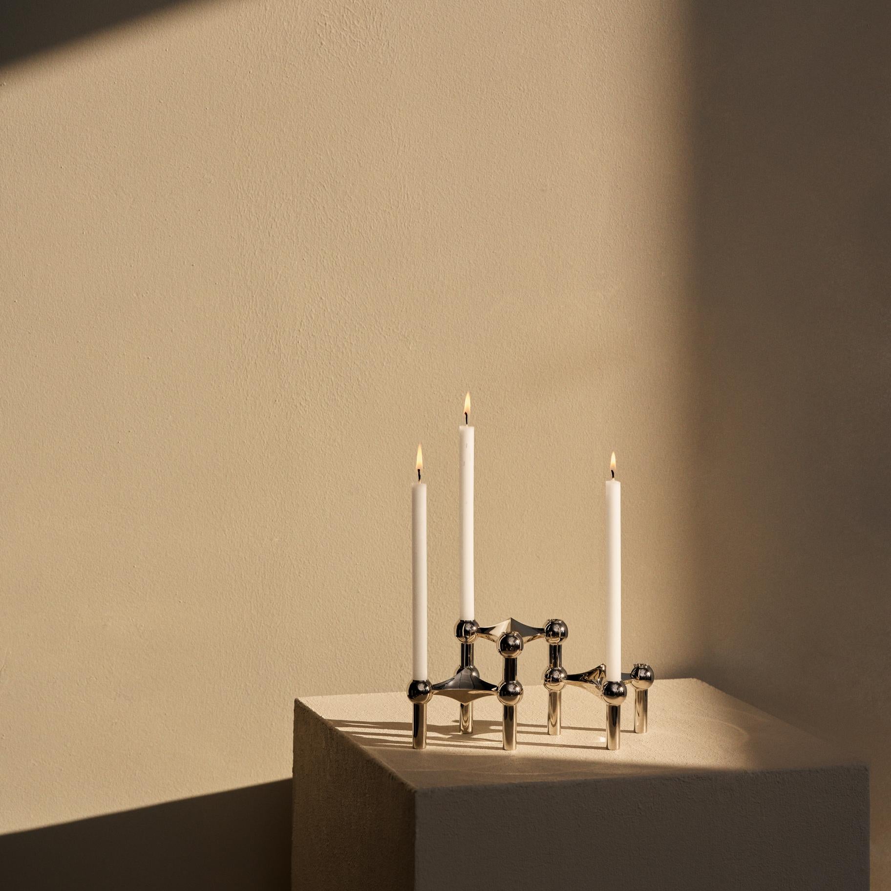 : STOFF Nagel chrome candle holders on a plinth holding three lit taper candles in a sunlit interior