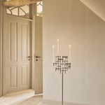 STOFF Nagel floor stand in chrome holding six BMF candle holders with lit taper candles, standing in a doorway of a modern interior