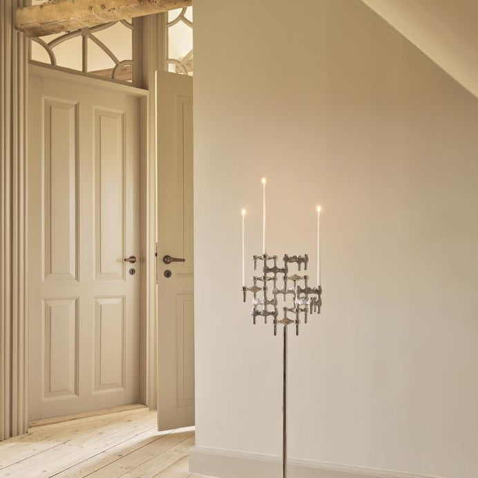 STOFF Nagel floor stand in chrome holding six BMF candle holders with lit taper candles, standing in a doorway of a modern interior
