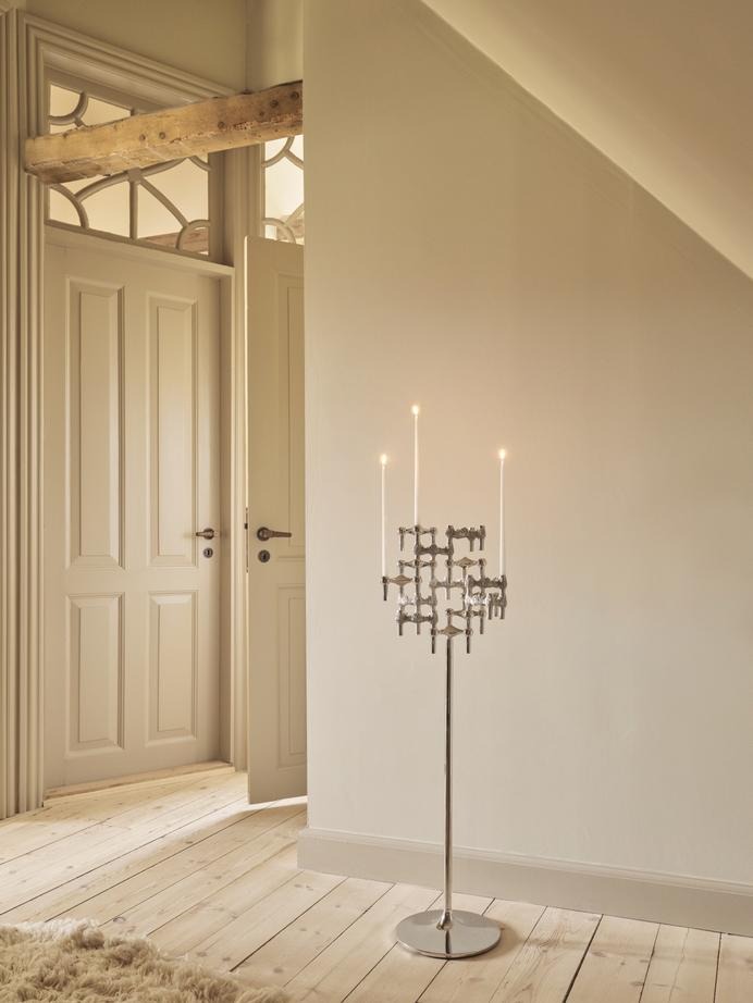 STOFF Nagel floor stand in chrome holding six BMF candle holders with lit taper candles, standing in a doorway of a modern interior