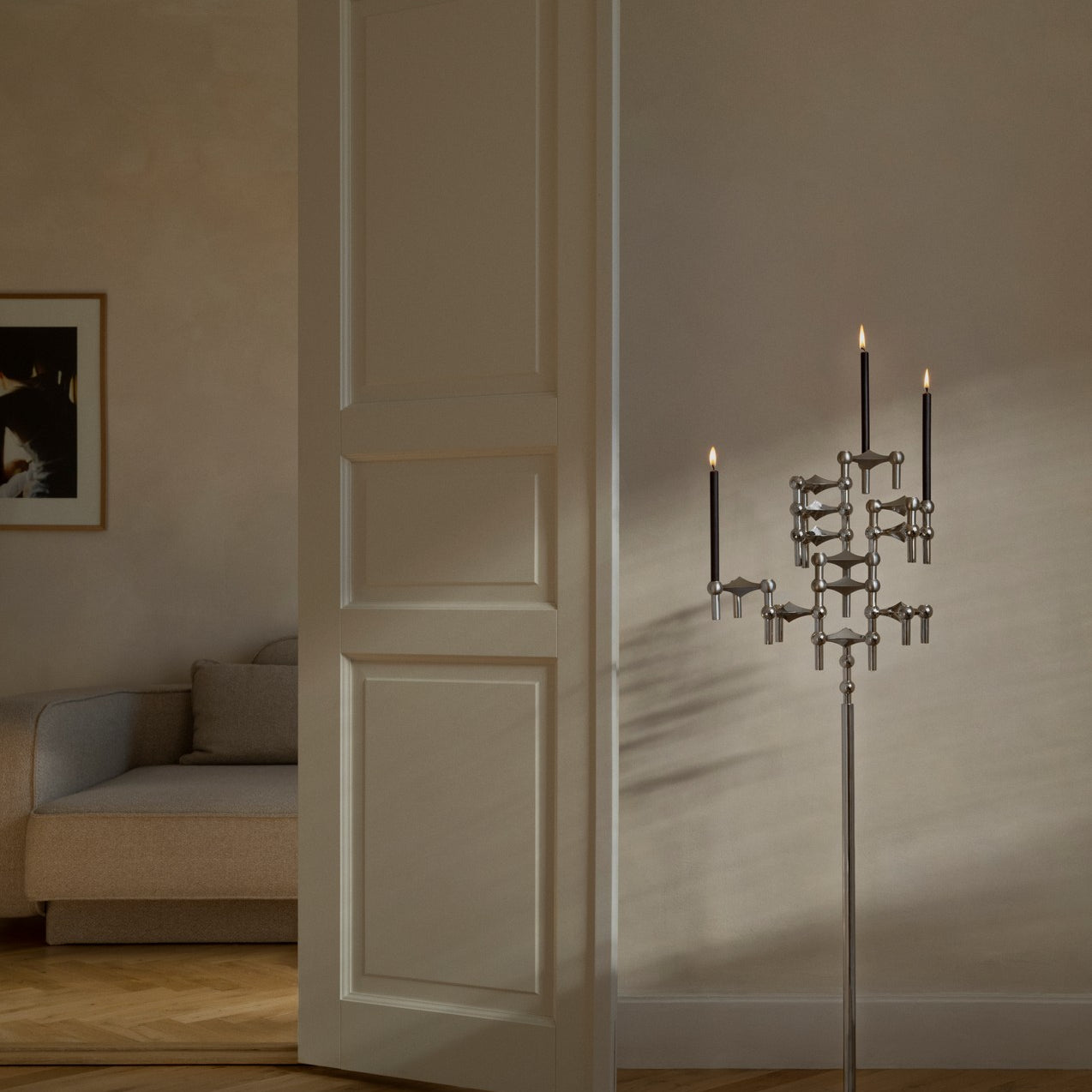 STOFF Nagel chrome floor stand with lit taper candles standing in a doorway of a modern living room