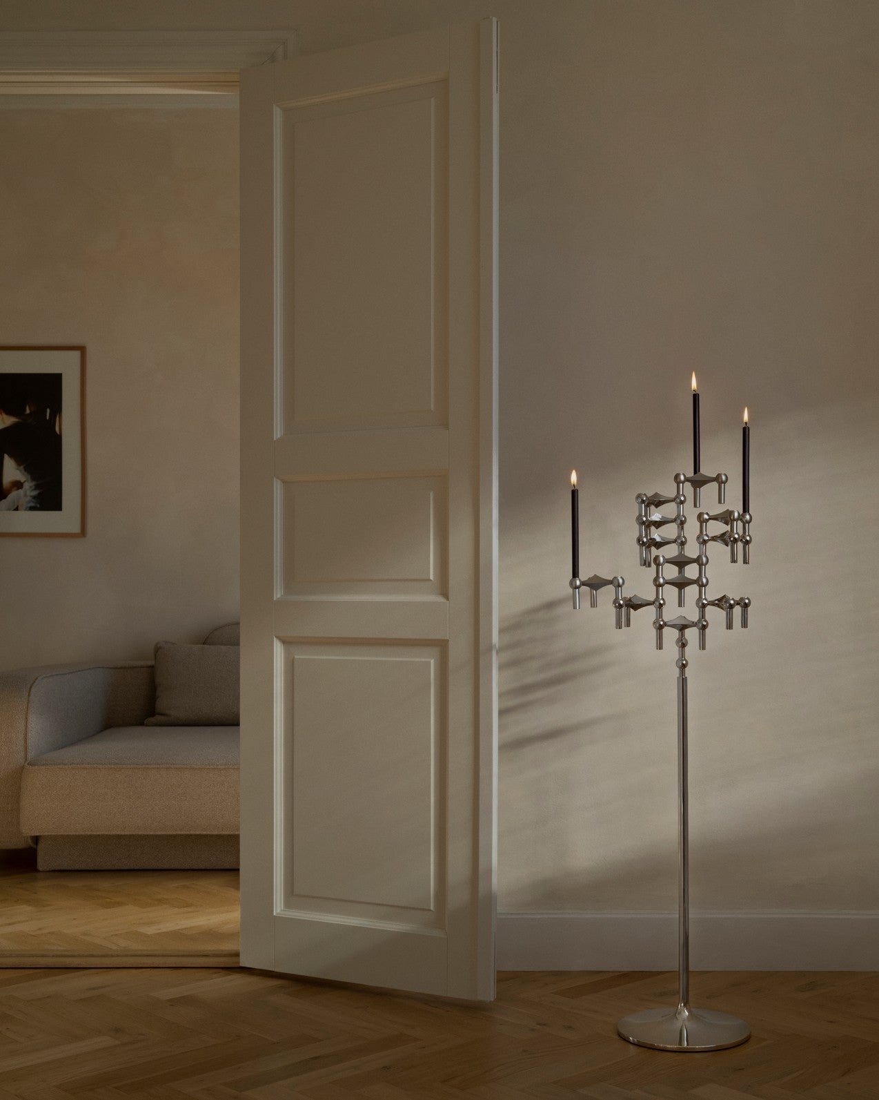 STOFF Nagel chrome floor stand with lit taper candles standing in a doorway of a modern living room