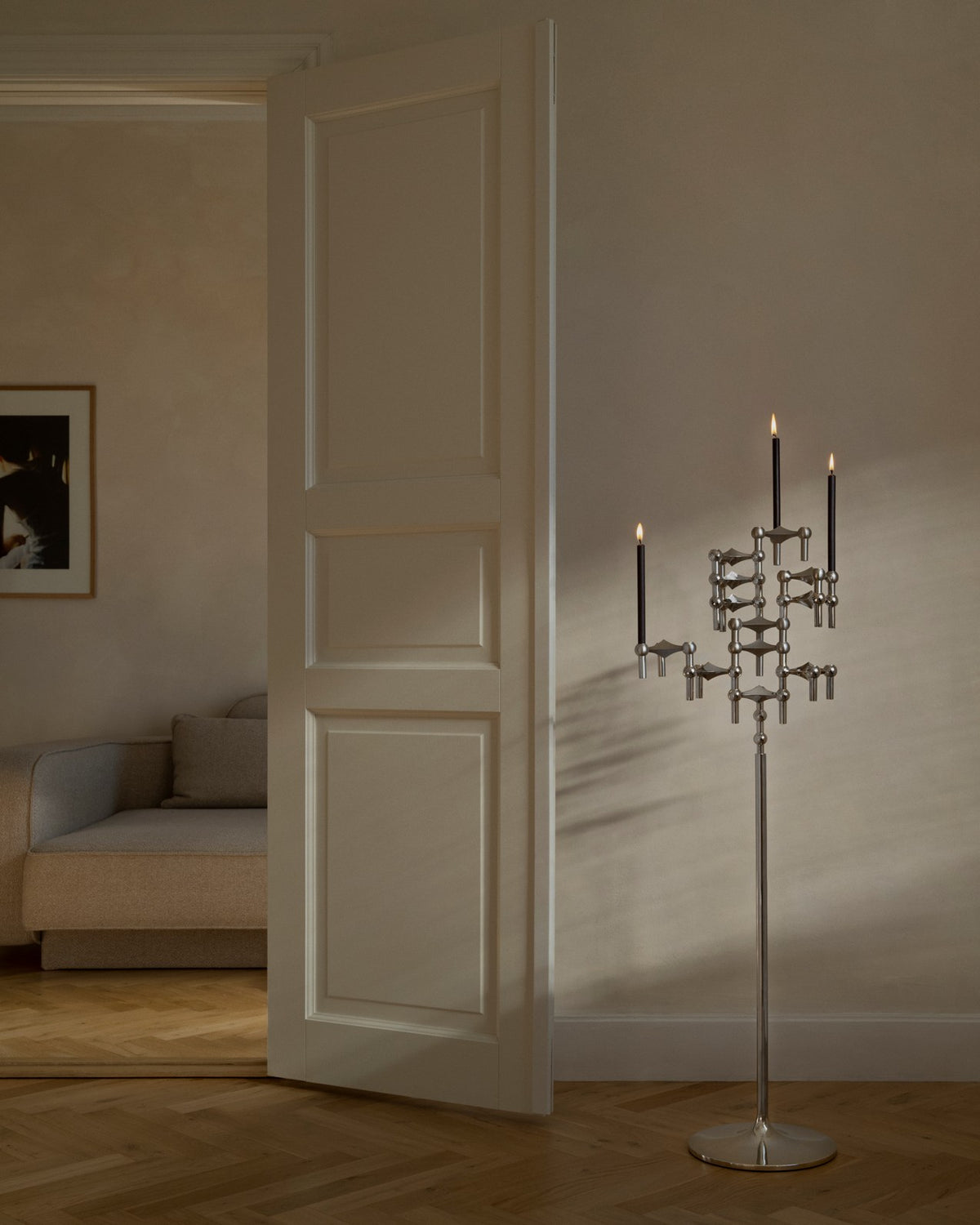 STOFF Nagel chrome floor stand with lit taper candles standing in a doorway of a modern living room