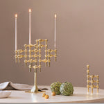 STOFF Nagel stand in solid brass built up with modular holders and lit taper candles, styled on a table with artichokes and linen