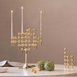 STOFF Nagel stand in solid brass built up with modular holders and lit taper candles, styled on a table with artichokes and linen