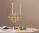 STOFF Nagel stand in solid brass built up with modular holders and lit taper candles, styled on a table with artichokes and linen