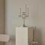 STOFF Nagel chrome stand holding lit taper candles on a plinth in a modern interior