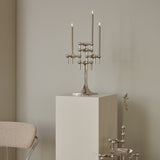 STOFF Nagel chrome stand holding lit taper candles on a plinth in a modern interior