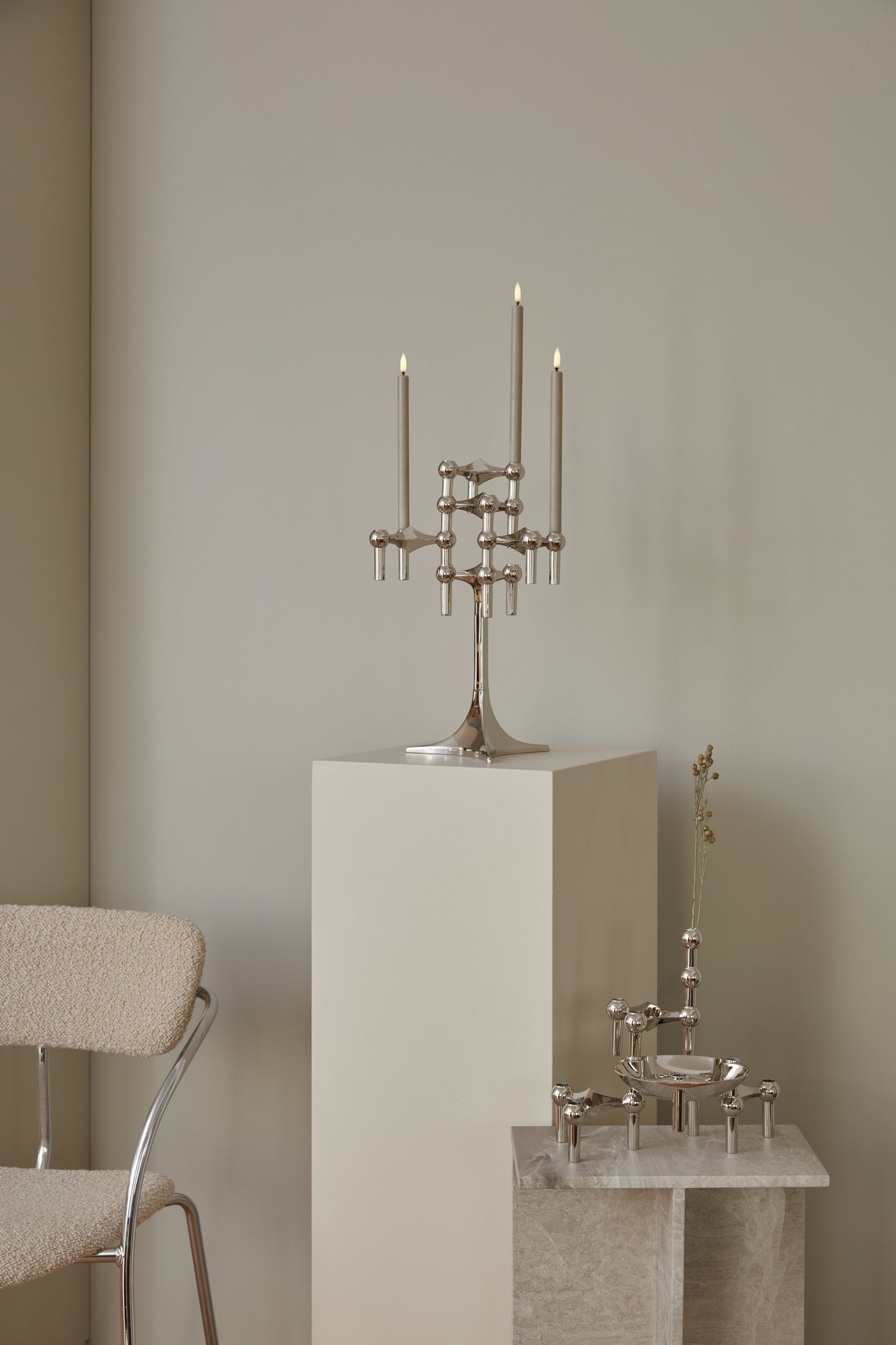 STOFF Nagel chrome stand holding lit taper candles on a plinth in a modern interior