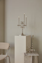 STOFF Nagel chrome stand holding lit taper candles on a plinth in a modern interior