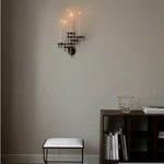STOFF Nagel black wall hanger mounted in a living room, holding lit taper candles above a bench and shelves