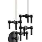 STOFF Nagel wall hanger in matte black holding a vertical arrangement of modular candle holders with lit taper candles